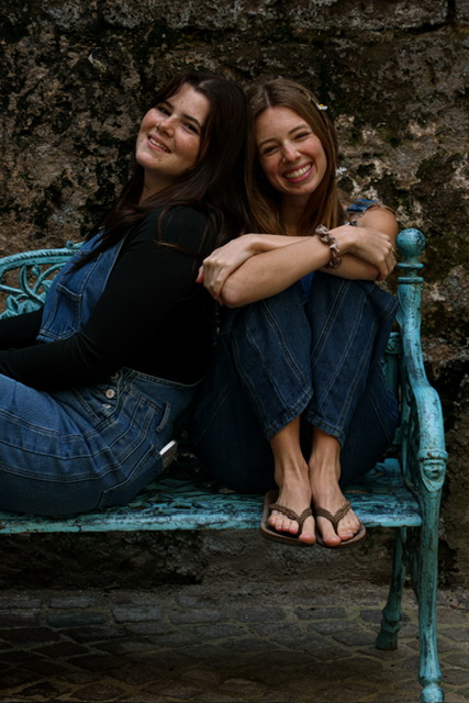 Two friends laughing together on a turquoise bench against a stone wall
