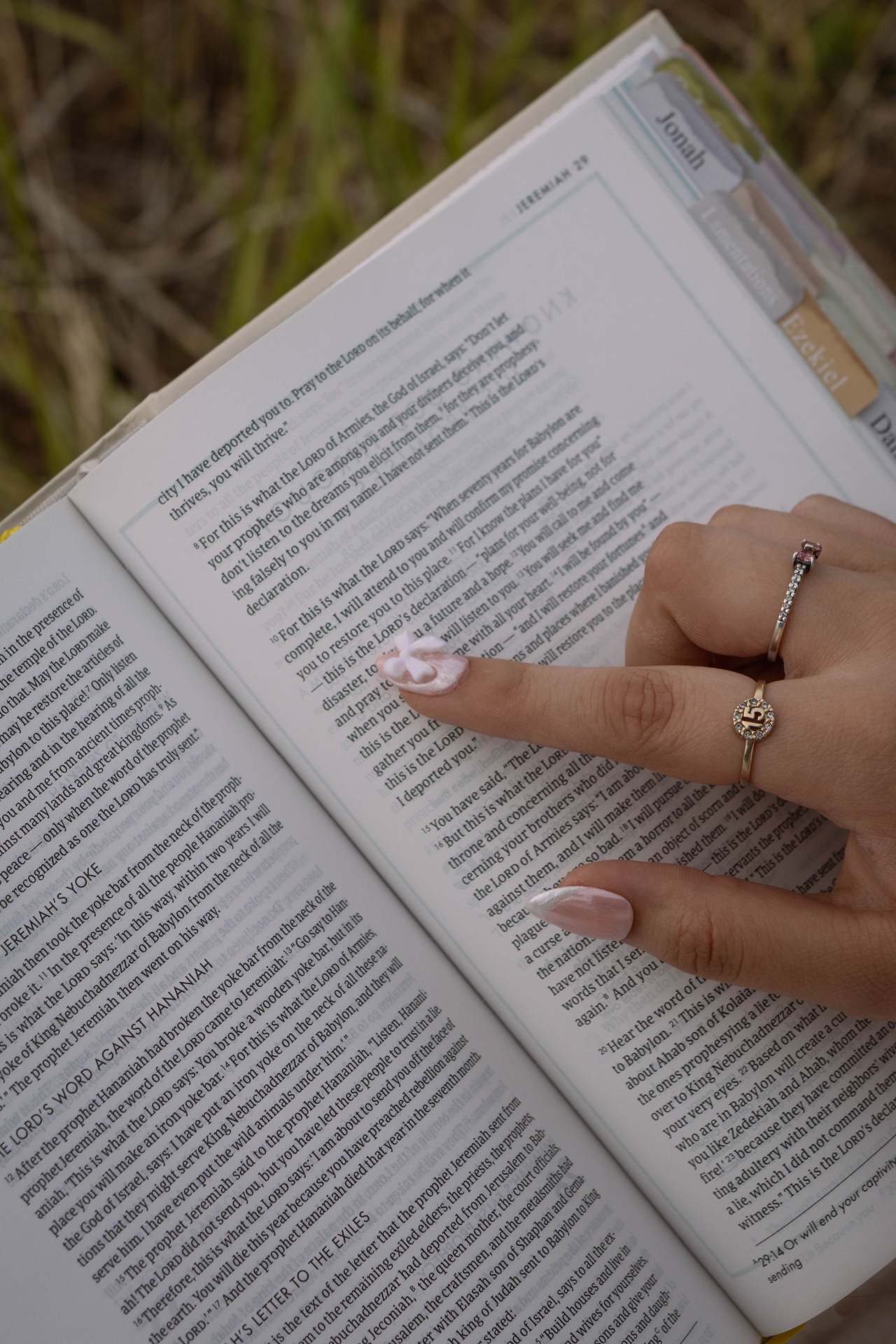 Hand with pink manicured nails resting on an open Bible in the grass