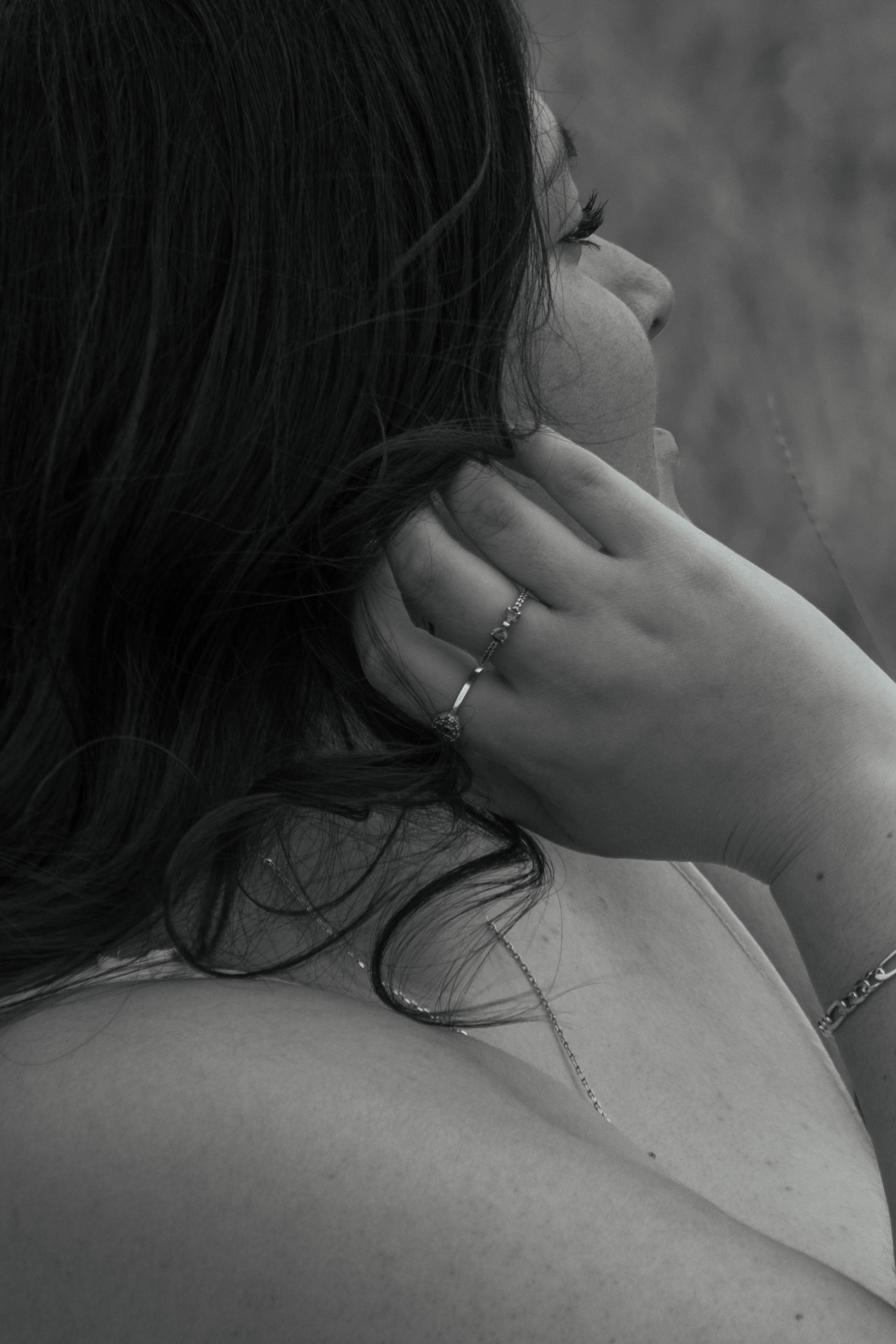 Black and white portrait from behind of a woman with dark hair, hand to her face