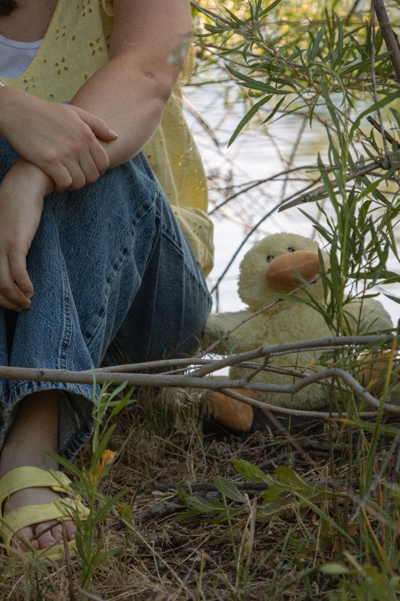 Detail of a girl sitting by the river with a plush duck tucked among willow branches