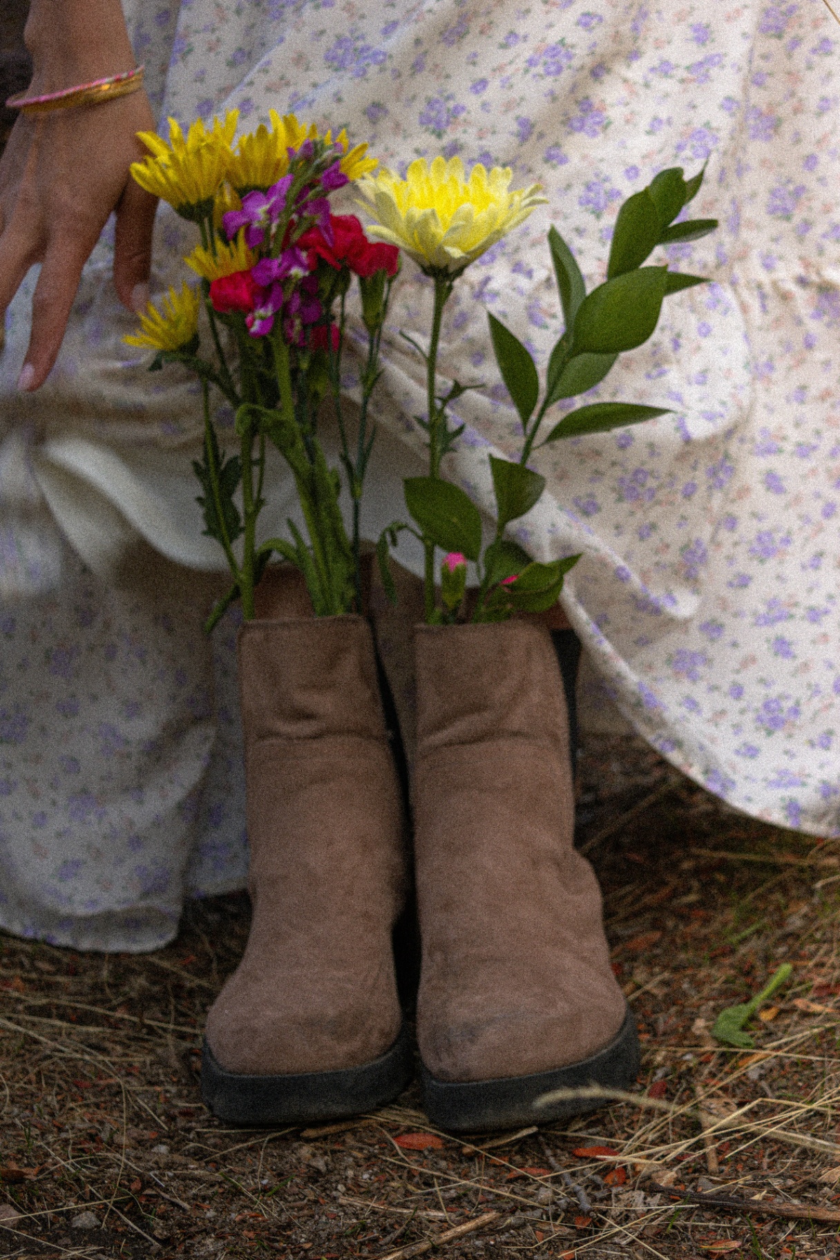 Detail of suede boots filled with a wildflower bouquet beside a floral dress