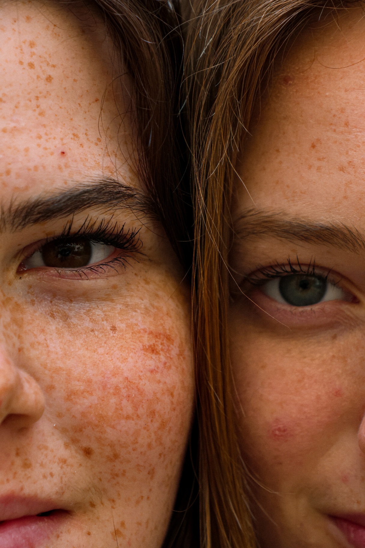 Extreme close-up of two friends' faces side by side, freckles and brown and blue eyes