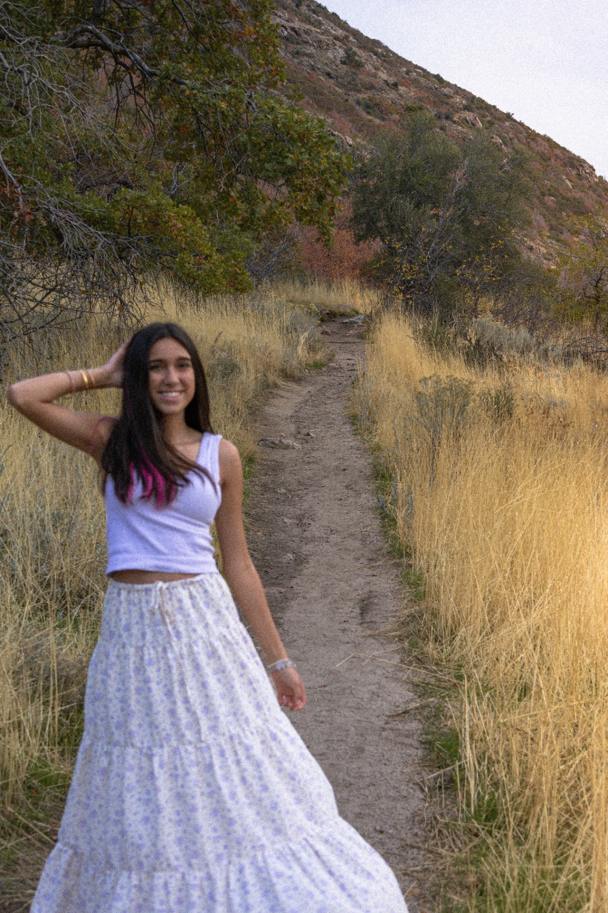 Izzy in a white tank and lavender floral skirt smiling on a foothills trail at golden hour