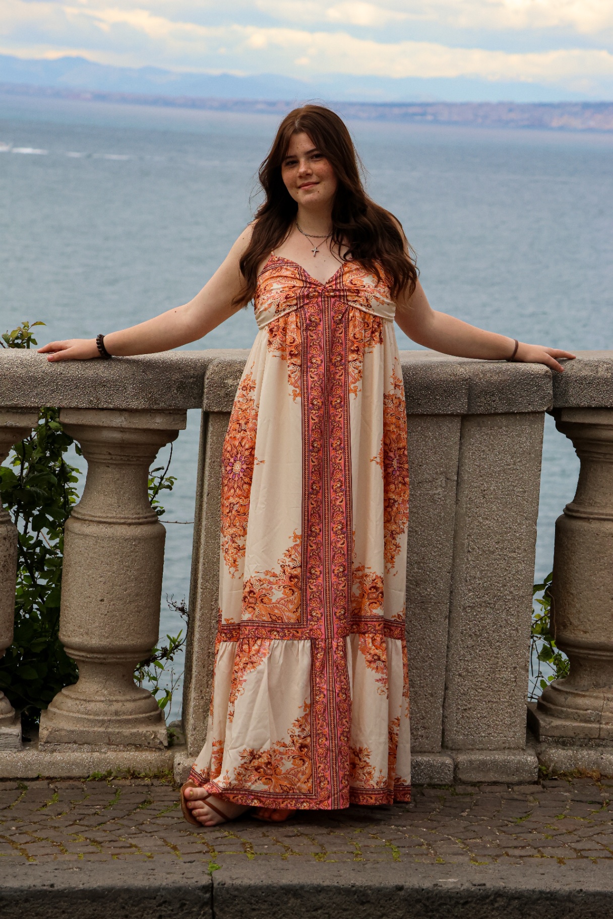 Young woman in floral maxi dress by the sea at golden hour